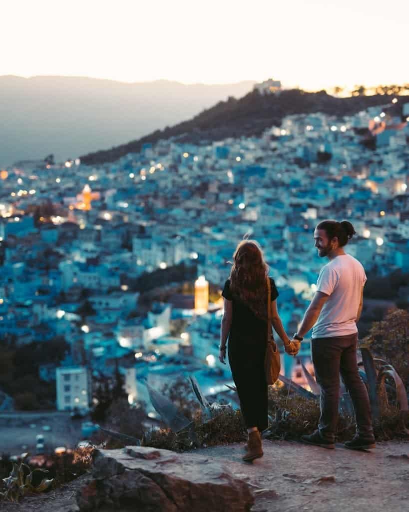 A romantic couple holding hands with a view of Chefchaouen, Morocco at twilight.