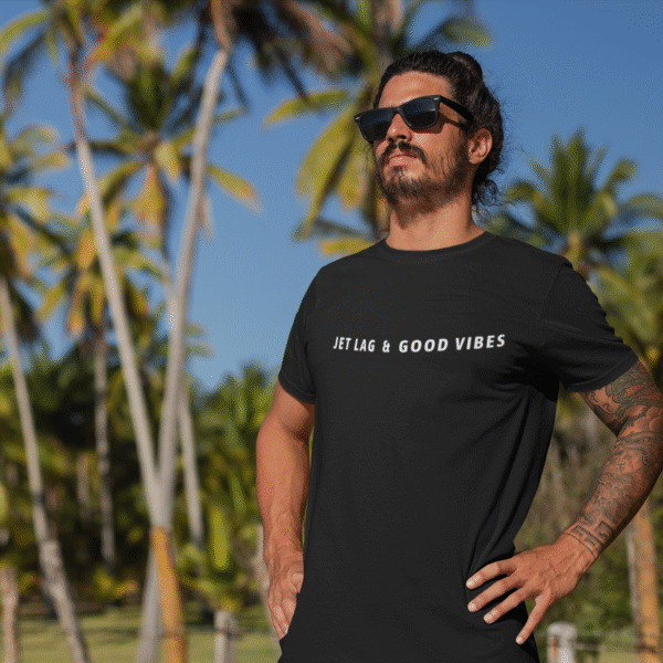 Man standing under palm trees wearing a black jetsetter tee with the text “Jet Lag & Good Vibes.”