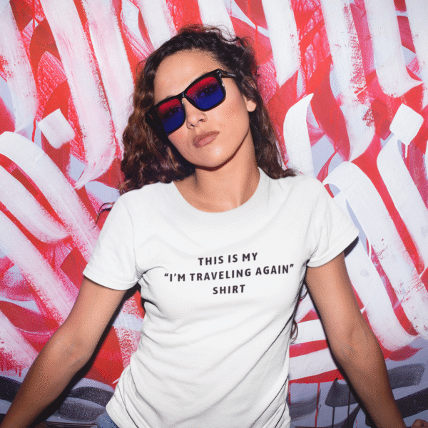 Woman wearing sunglasses and a white women’s travel t-shirt with the text “This Is My I’m Traveling Again Shirt.”