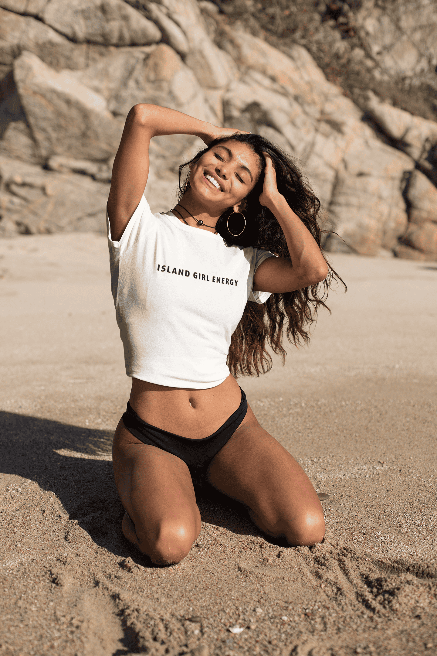 Woman smiling on the beach wearing a white island vibes t-shirt with the text “Island Girl Energy.”