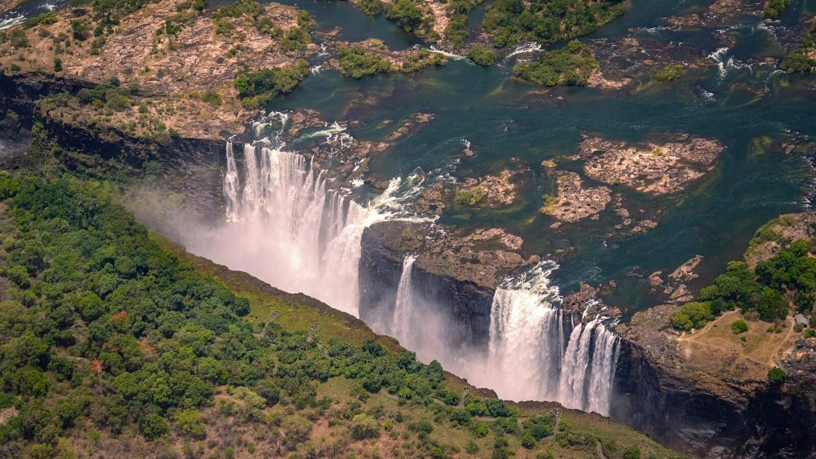 Breathtaking aerial view of Victoria Falls surrounded by lush greenery during summer day Natural Wonders